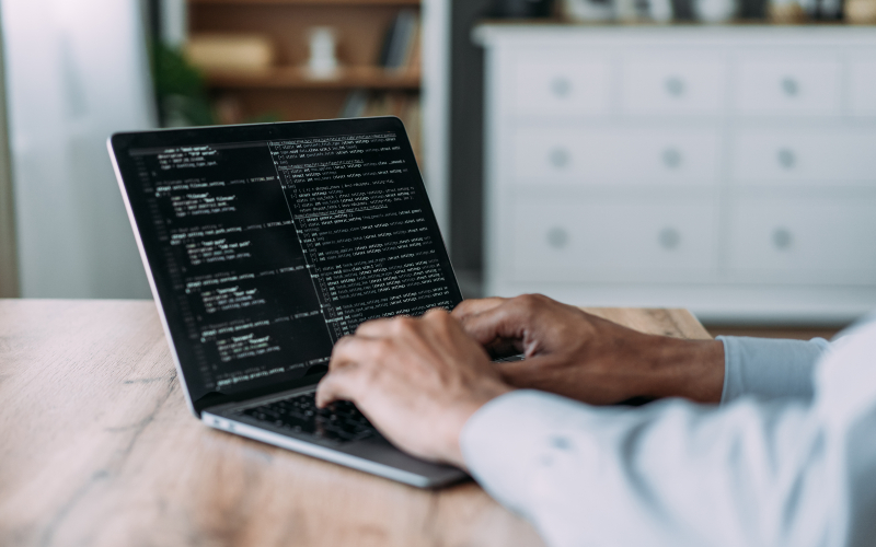 Hands typing on a laptop with a black screen and white writing