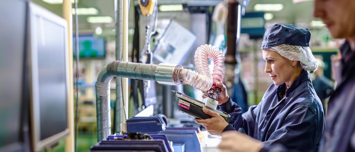 Woman in factory holding a Brother cartridge in her left hand and machinery in her right